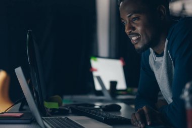 genç afro-amerikan programcı ofiste gece bilgisayar monitörü bakarken gülümseyen