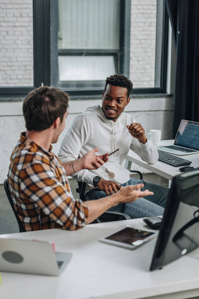 two cheerful multicultural programmers discussing ideas while sitting together in office