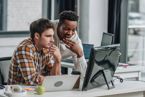 two thoughtful multicultural programmers looking at computer monitor while working in office together