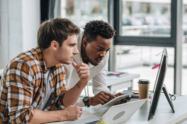 african american programmer using digital tablet while working with colleague in office