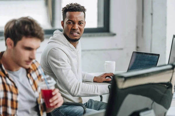 选择性的焦点愤怒的非洲裔美国程序员坐在附近周到的同事 — 图库照片