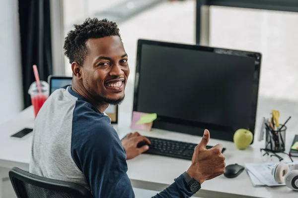 쾌활한 아프리카 미국인 프로그래머가 카메라를보고 컴퓨터 근처에 앉아있는 손가락을 보입니다 — 스톡 사진