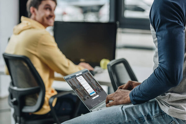 KYIV, UKRAINE - JULY 29, 2019: partial view of african american programmer using laptop with Linkedin website on screen near smiling colleague
