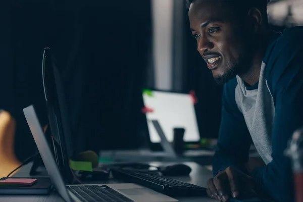 Joven Programador Afroamericano Sonriendo Mientras Mira Monitor Computadora Por Noche — Foto de Stock