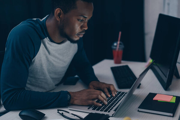 attentive african american programmer using laptop while working at night in office