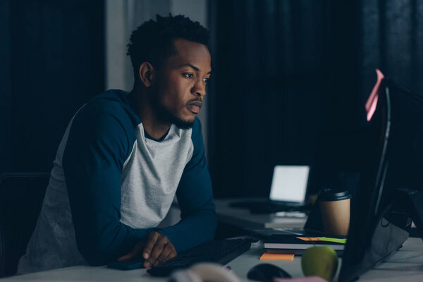 thoughtful african american programmer working at night in office