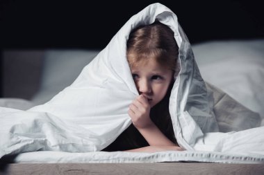 frightened child hiding under blanket and looking away isolated on black clipart