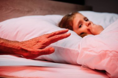 korkmuş çocuk yanında erkek el yatakta yatan ve sus işareti gösteren
