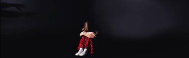 panoramic shot of depressed child sitting with bowed head on black background clipart