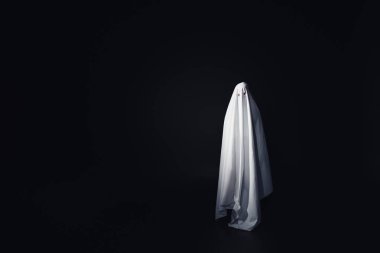 frightening ghost in white bedsheet isolated on black with copy space clipart
