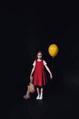 sarı balon ve oyuncak ayı ile üzgün, yalnız çocuk siyah izole kamera bakıyor