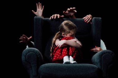 scared child sitting in armchair surrounded with human hands isolated on black clipart