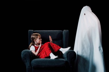 direful ghost standing near scared girl sitting in armchair isolated on black clipart