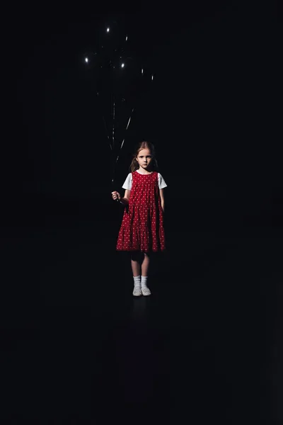 黒い風船で立って 黒で隔離されたカメラを見て悲しい子供 — ストック写真