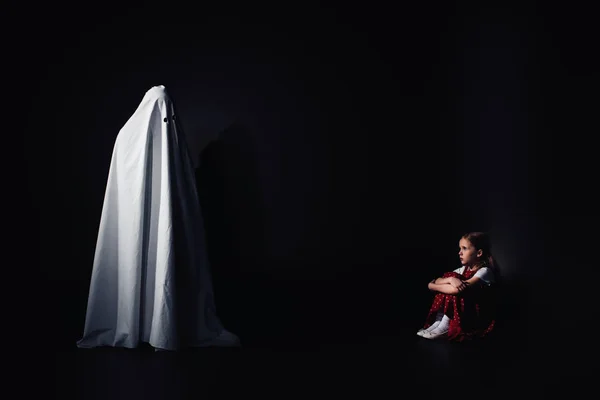 Niño Asustado Sentado Suelo Mirando Terrible Fantasma Blanco Sobre Fondo —  Fotos de Stock