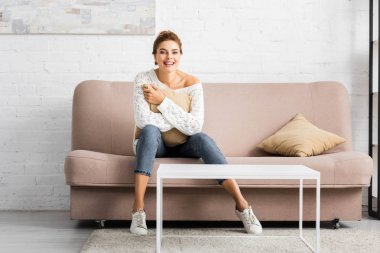 beyaz kazak yastık tutan ve kameraya bakarak çekici kadın 