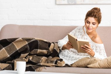 beyaz kazak çekici kadın kanepede oturan ve kitap okuma 