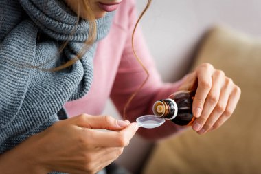 cropped view of ill woman with grey scarf taking cough syrup   clipart