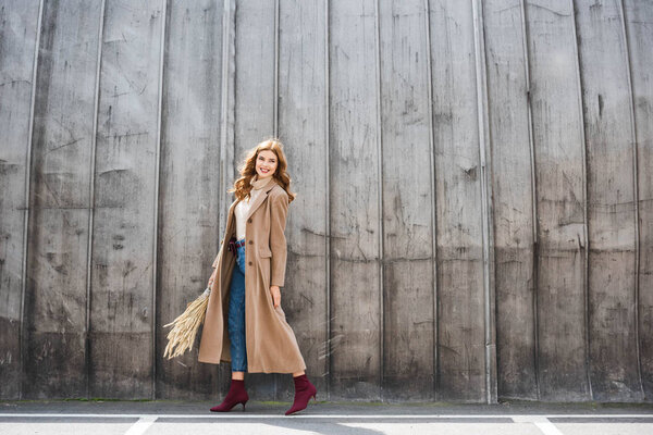 attractive and smiling woman in coat holding spikes and looking away 