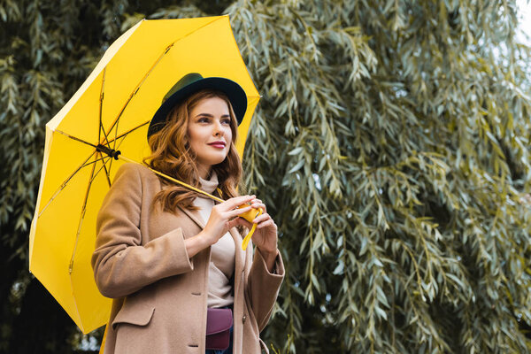 attractive woman in blue hat looking away and holding yellow umbrella 