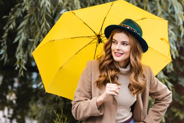 青い帽子をかぶった魅力的な女性が目をそらし 黄色い傘を持っている — ストック写真