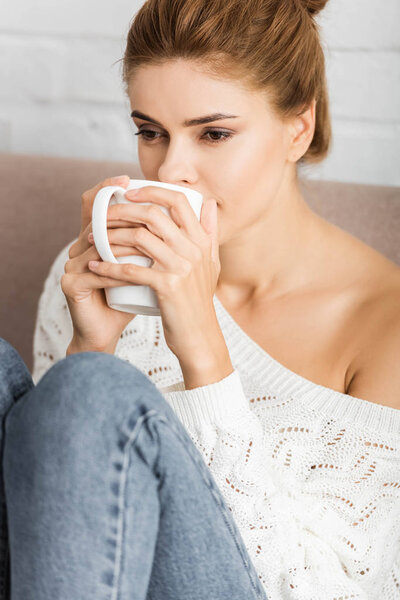 attractive woman in white sweater holding cup and looking away 