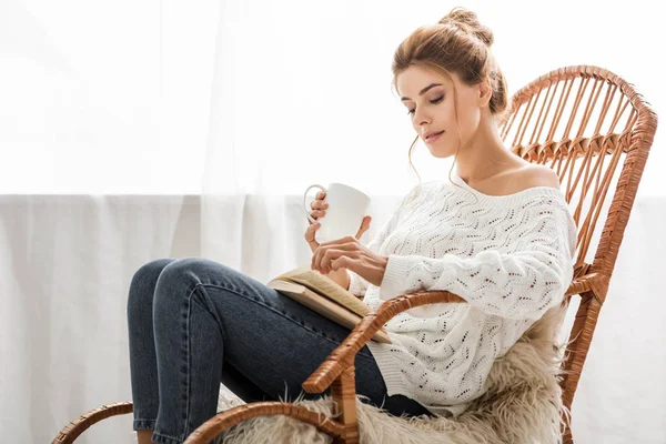 穿着白色毛衣的迷人女人坐在摇椅上看书 — 图库照片