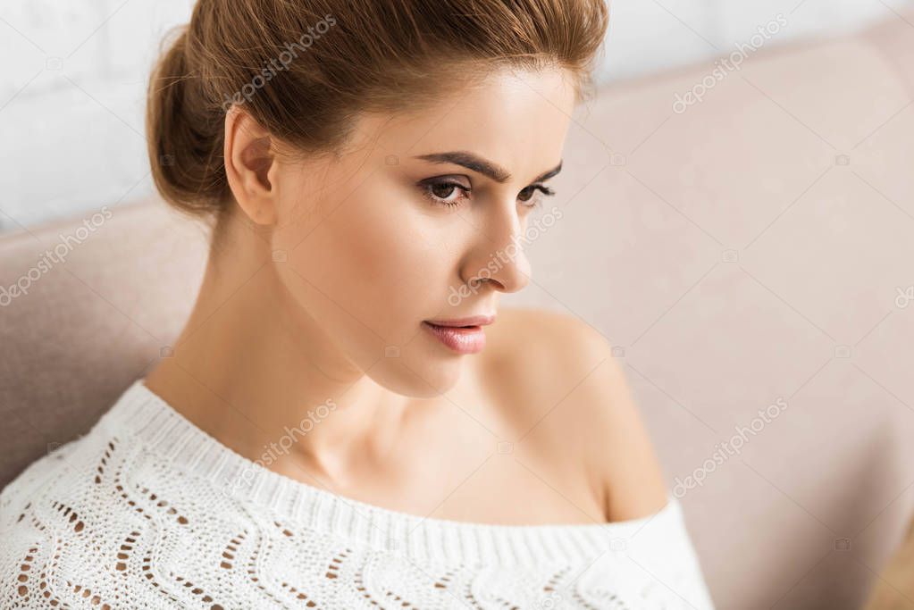 attractive woman in white sweater looking away in apartment 