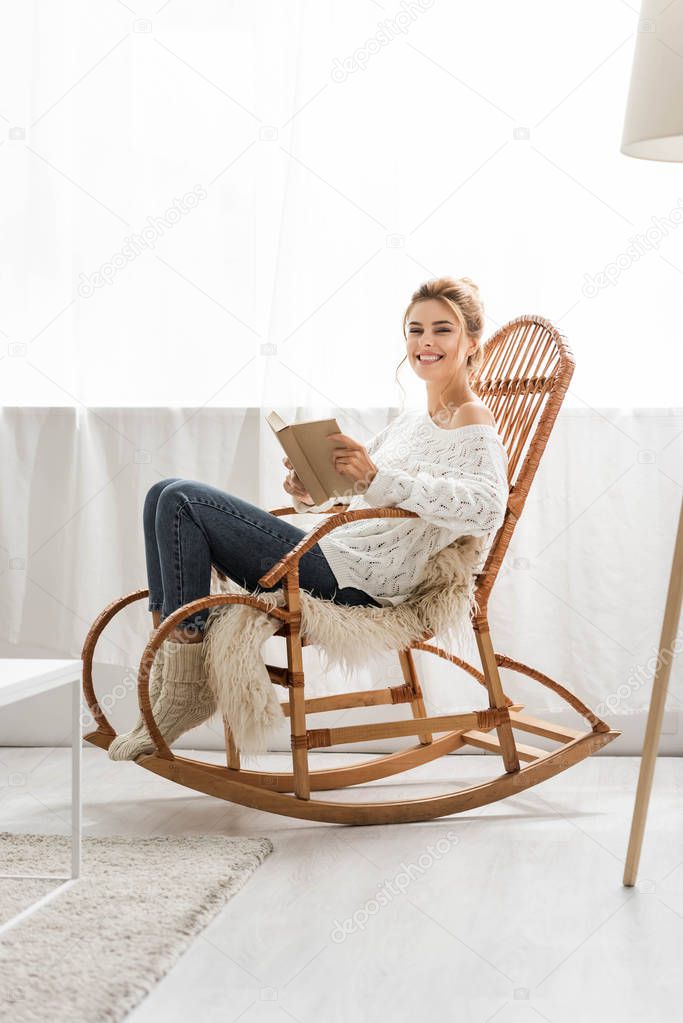 attractive woman in white sweater sitting on rocking chair and holding book