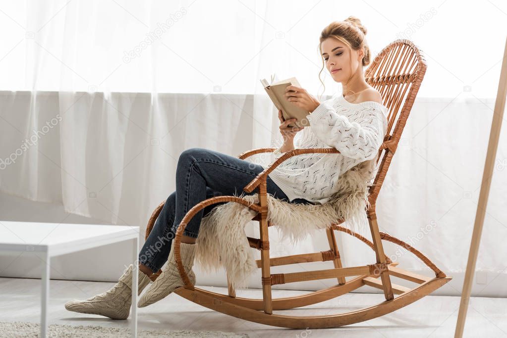 attractive woman in white sweater sitting on rocking chair and reading book