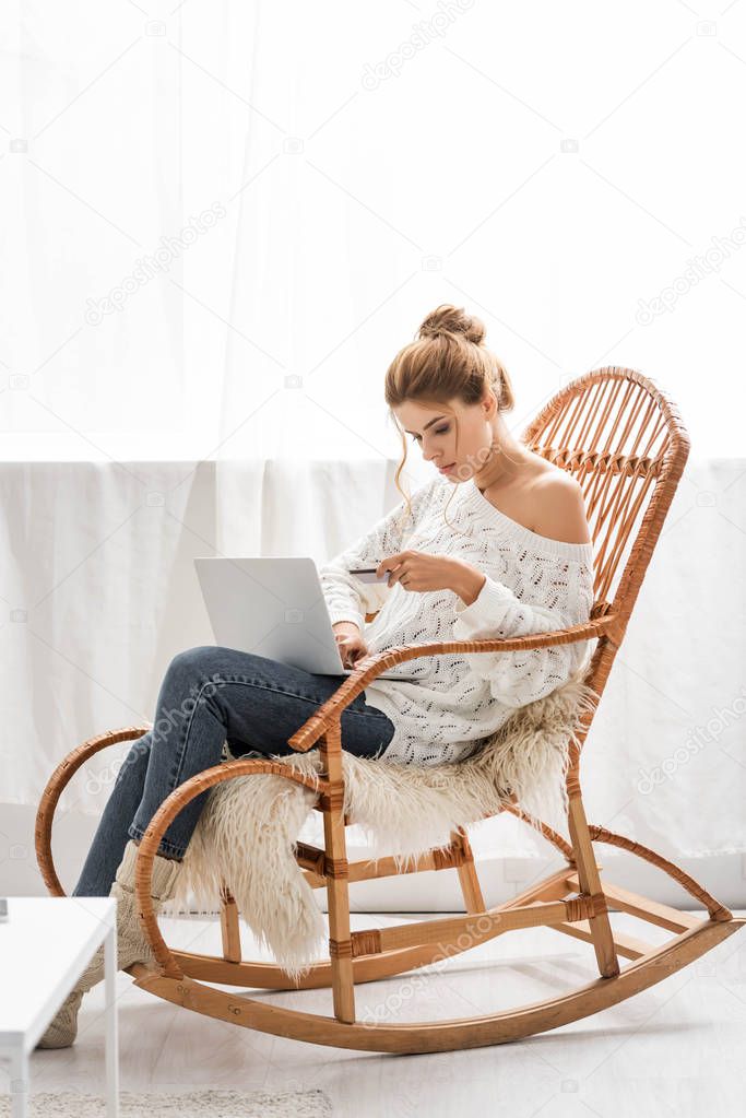 attractive woman in white sweater holding credit and laptop
