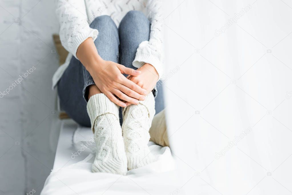 cropped view of woman in white sweater and jeans sitting in apartment 