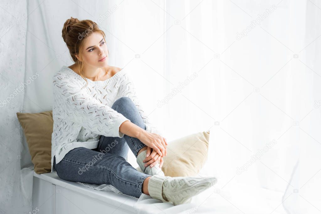attractive woman in white sweater and jeans sitting and looking away 