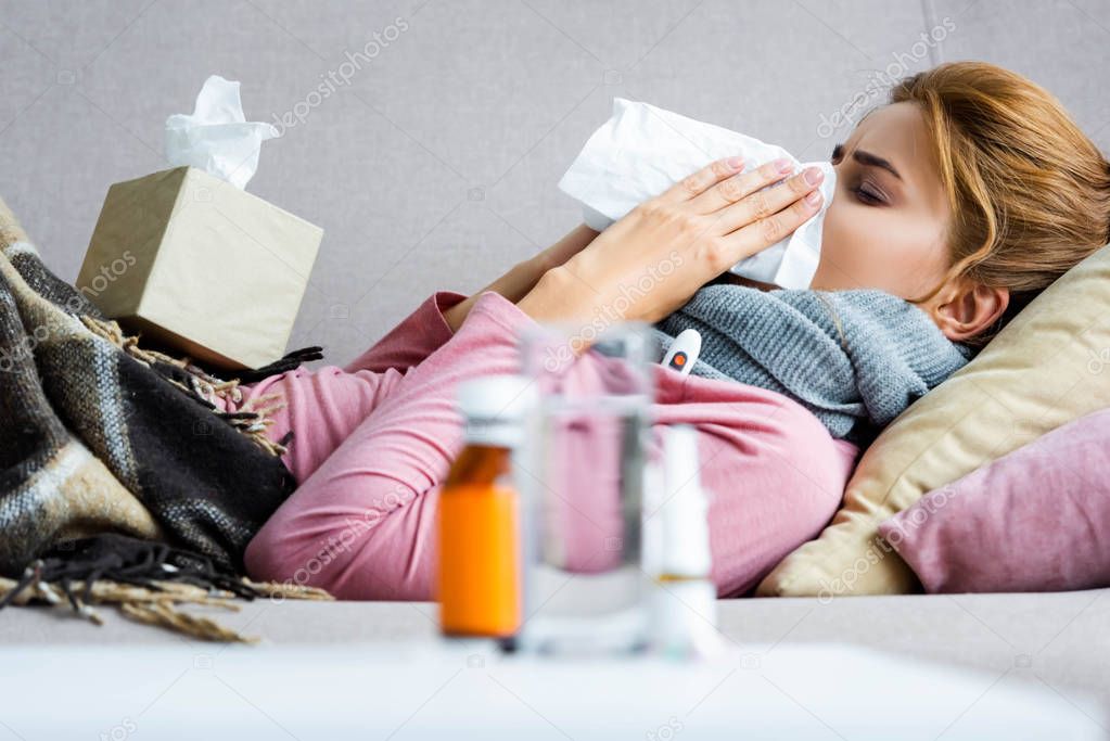 selective focus of attractive and ill woman sneezing and using napkin 