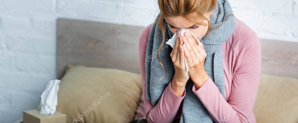 Панорамный снимок больной женщины с серым шарфом чихающей и с помощью салфетки