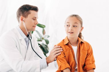stetoskoplu çocuğu inceleyen beyaz önlüklü pediatrist