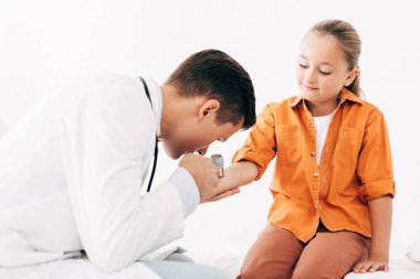 dermaskoplu çocuğu inceleyen beyaz önlüklü pediatrist