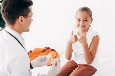 pediatrist tutarak şırınga ve gülümseyen çocuk başparmak gösteren