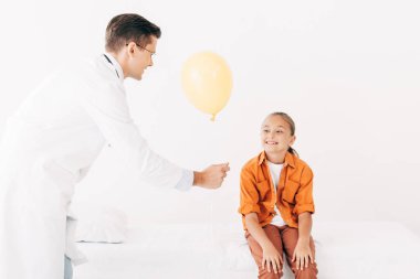 klinikte çocuğa sarı balon veren beyaz ceketli pediatrist