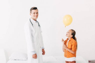 beyaz önlük ve klinikte balon ile mutlu çocuk gülümseyen pediatrist
