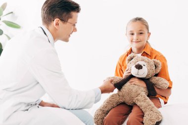 beyaz önlük ve çocuk klinikte oyuncak ayı ile gülümseyen pediatrist