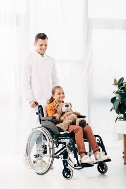 beyaz önlük ve tekerlekli sandalyede oyuncak ayı ile çocuk pediatrist tam uzunlukta görünümü