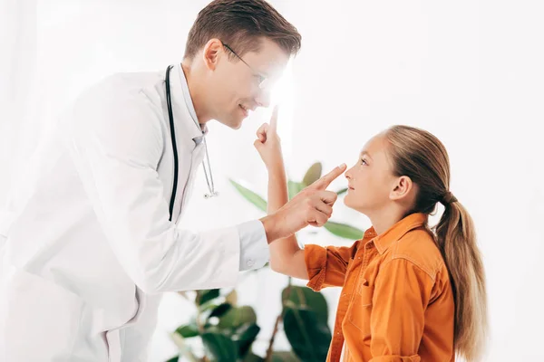 白いコートを着た笑顔の小児科医と クリニックでお互いを見つめ合う子供 — ストック写真