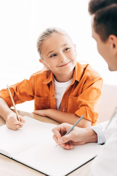 微笑的孩子和医生在笔记本上写在诊所的桌子上 — 图库照片