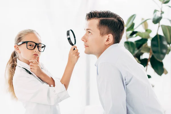 Peinzende Kind Doctor Kostuum Onderzoek Patiënt Met Vergrootglas — Stockfoto