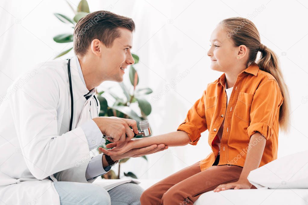 smiling pediatrist in white coat examining child with dermascope