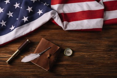 top view of leather notebook, telescope, nib and compass on wooden surface with American national flag clipart