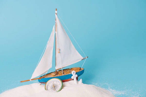 decorative ship near anchor and compass in white sand on blue background