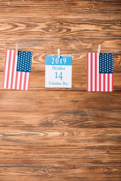 calendar paper sheet with 14 October date between American national flags on wooden surface