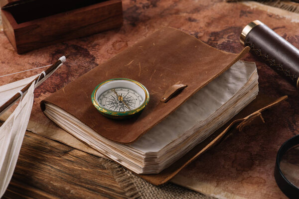 brown leather notebook with compass on wooden surface with world map